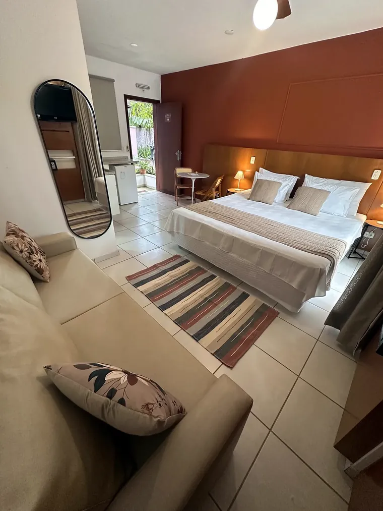 Estúdio Varanda com sofá, espelho de corpo inteiro e cama ao fundo