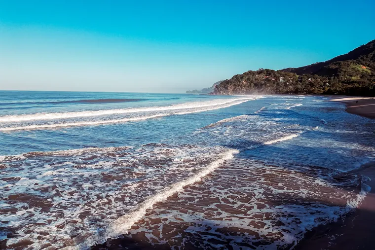 Ondas quebrando na areia da Barra do Sahy com a serra ao fundo