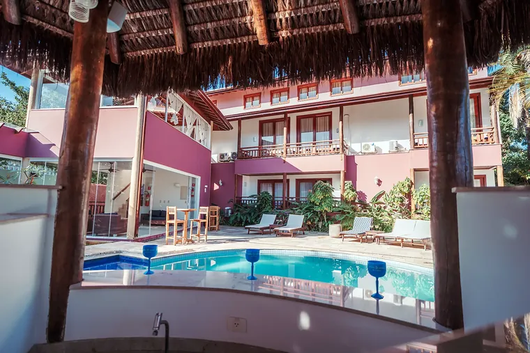 Piscina vista de dentro do bar de sapê, com taças na bancada