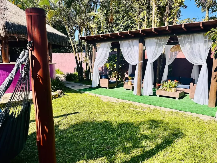 Lounge de cortinas visto do jardim, com rede em primeiro plano